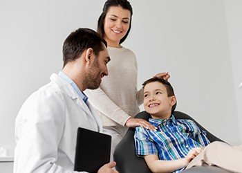 Smiling child in dental office with parent and dentist