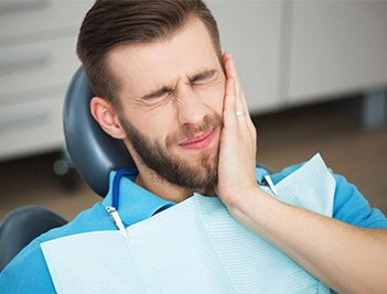 Man in dental chair holding cheek